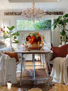 Cement pumpkin bowl sits on wood table, filled with flowers and surrounded by candles.