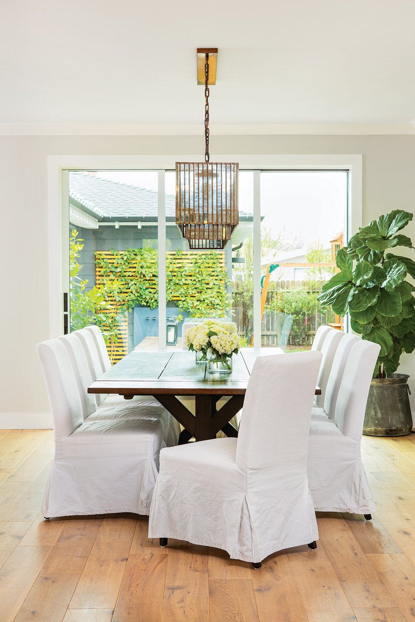 dining area with large coastal patio doors, a long dark wooden table and 8 chairs with white chair covers