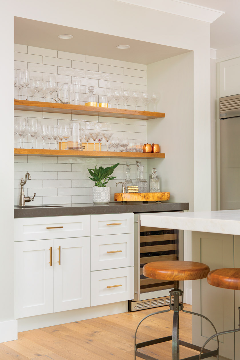 white kitchen with white subway tile, open natural wood shelving adorned with glassware, brass hardware and gray countertops