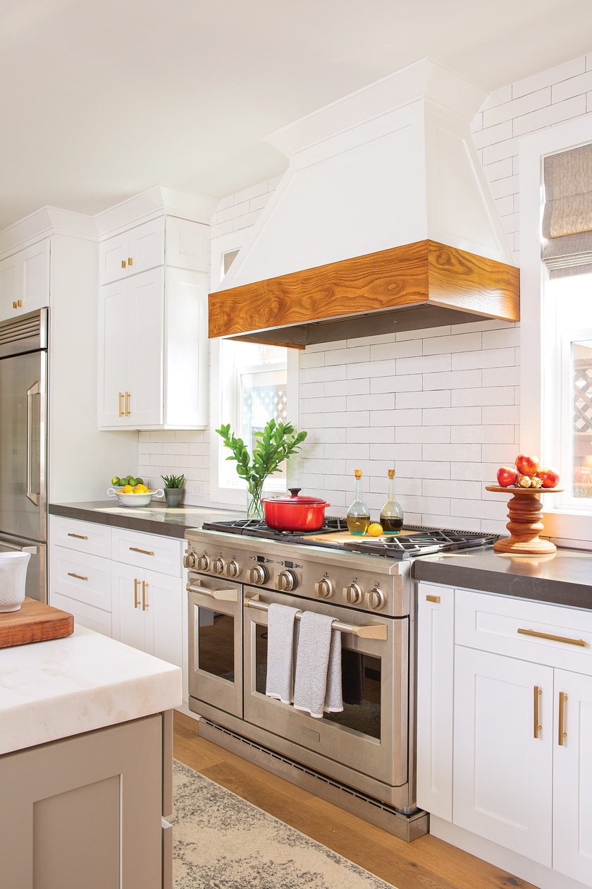 white kitchen with stainless steel double wide stove with white and natural farmhouse wood hood above stove 