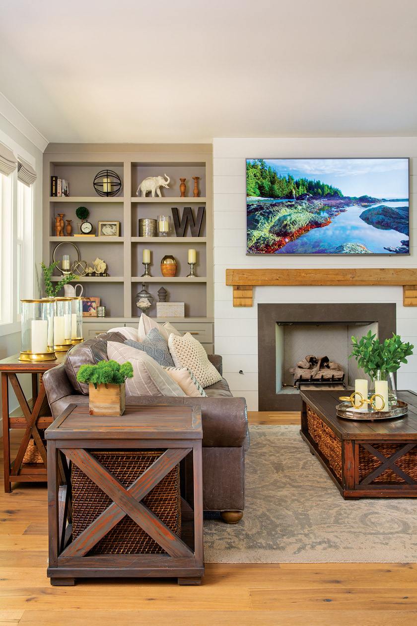 family room with fireplace, tv above mantel, open shelving with decor, fluffy pillows on the sofa an decorative lanterns on a sofa table 