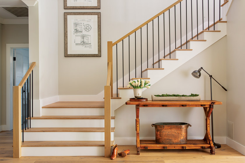 white and natural wood coastal farmhouse style open stairway with neutral wall art and small table with accessory at base of stairs 