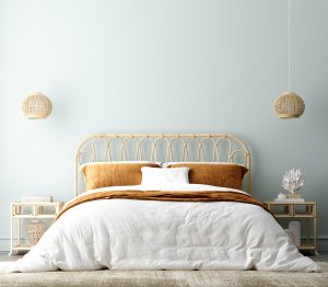 This boho coastal bedroom mixes neutral textures that complement both styles. The blue wall and sculpture read coastal, while the lighting and headboard have a boho feel. [Photo courtesy of iStock/Artjafara]