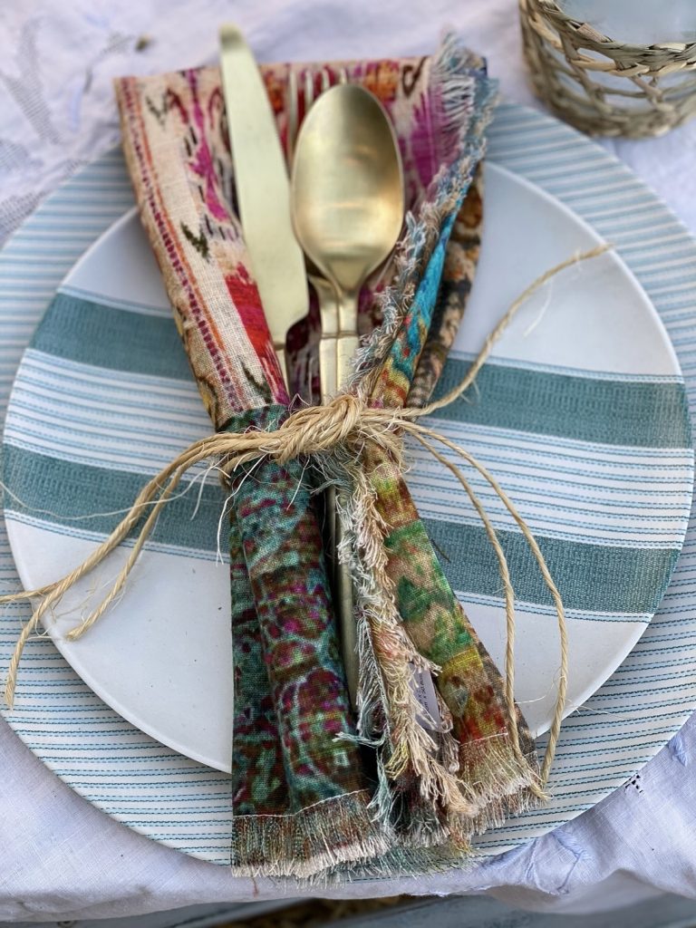 Each place setting includes a combo of striped plates, rattan-covered glasses, colorful cloth napkins and gold silverware, for lots of added texture.