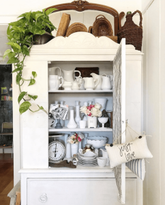 A dining room cabinet with a hand embroidered pillow hanging from the open door