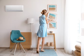air conditioner on wall next to woman in blue dress hanging pictures