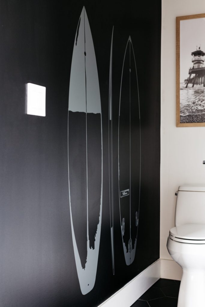 Modern beach home bathroom with black accent wall and painted surfboards