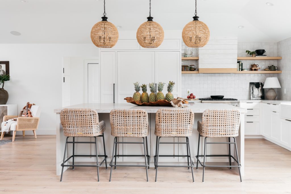 White kitchen with rattan bar stools and hanging pendant lights in modern beach home