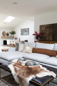 White couch with tan throw pillows and black leather ottoman table in modern beach home