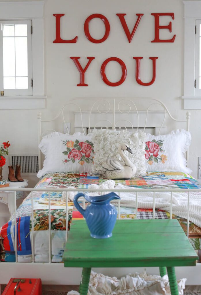 A bedroom with floral bedding, a green table, and a blue vase