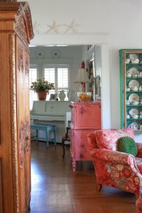 A sitting room with a pink floral chair and a pink vintage cabinet