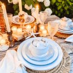 Beach table setting with white ceramic dishes, tea candles, white shells, and rattan chargers