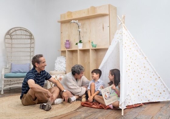 A couple plays with two small children with a tent in a playroom.