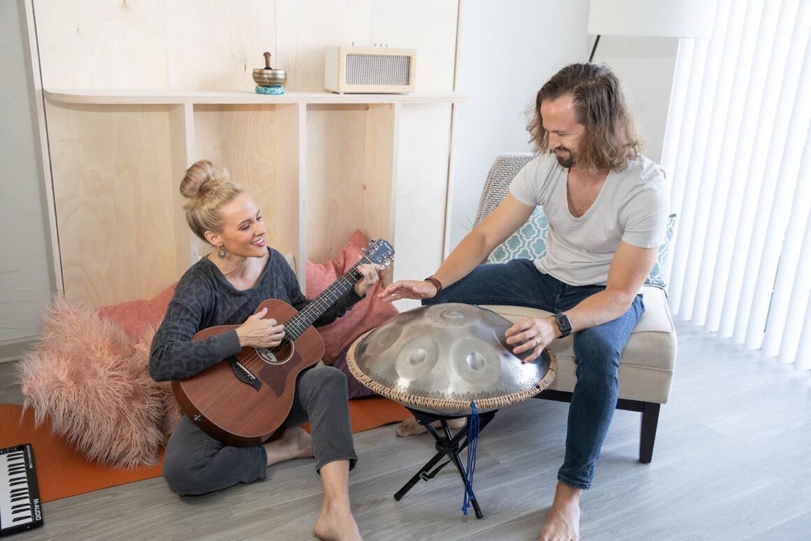 A man and woman playing a guitar and steel drum in front of their Lori Murphy bed.