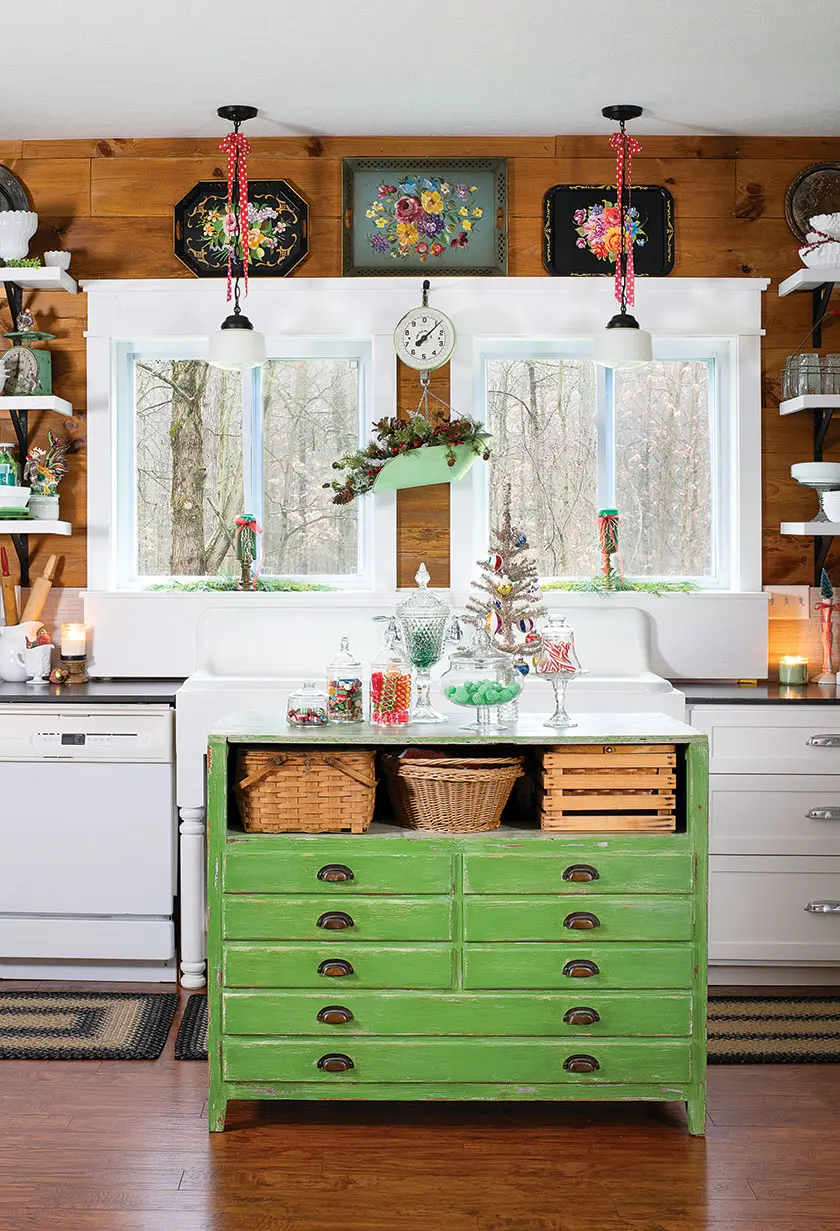holiday kitchen with vintage green island, fresh greenery and red and white ribbon on lighting fixtures