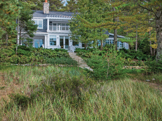 cottage alongside Lake Michigan with cedar shake shingles blue siding white trim and river rock chimney