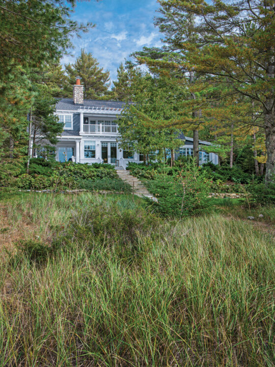 cottage alongside Lake Michigan with cedar shake shingles blue siding white trim and river rock chimney