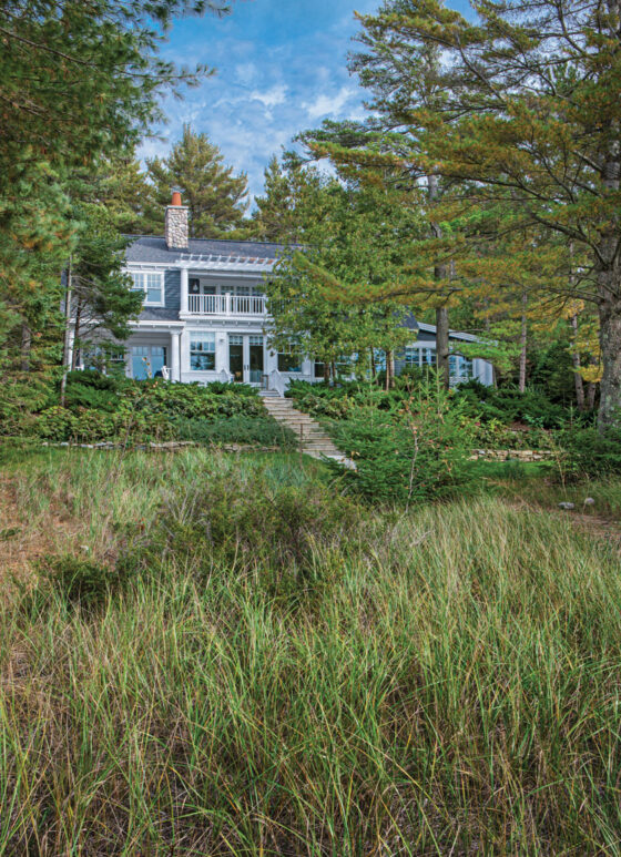 cottage alongside Lake Michigan with cedar shake shingles blue siding white trim and river rock chimney