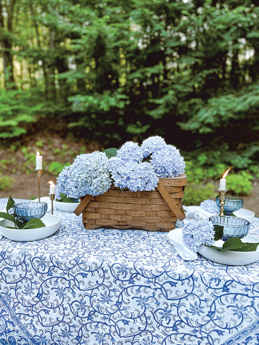 blue hydrangeas in picnic basket as centerpiece on outdoor dining table with blue and white color scheme