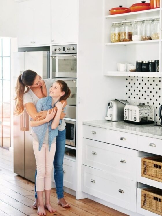 A woman with a kid with hug in a kitchen with some appliances