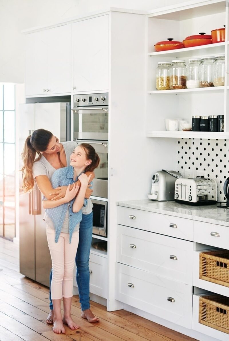 A woman with a kid with hug in a kitchen with some appliances