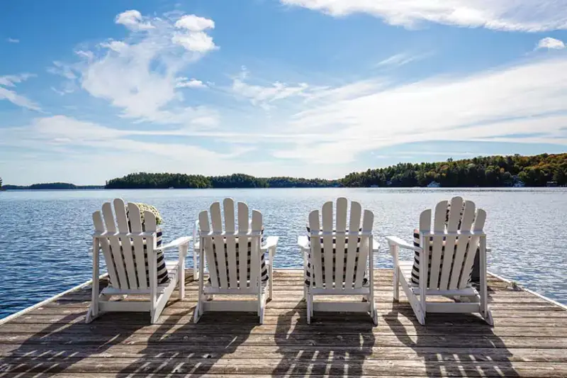 white Muskoka chairs on dock overlooking Lake Muskoka