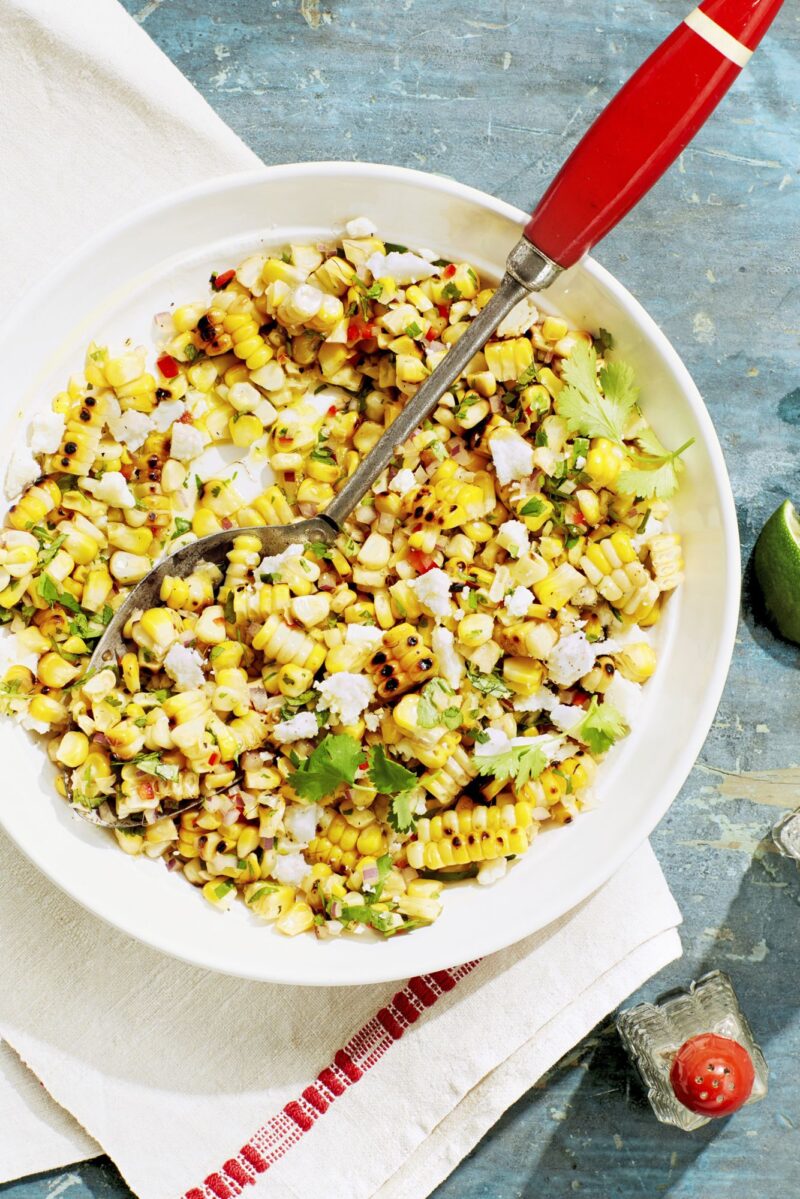 charred corn salad in a white bowl and with a red color spoon
