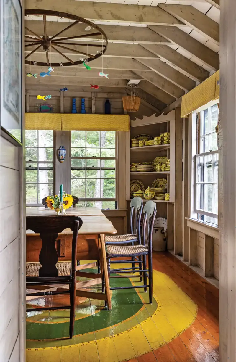Maine cottage with wagon wheel mobile above dining room table and wood floor painted in multi-colored rug design
