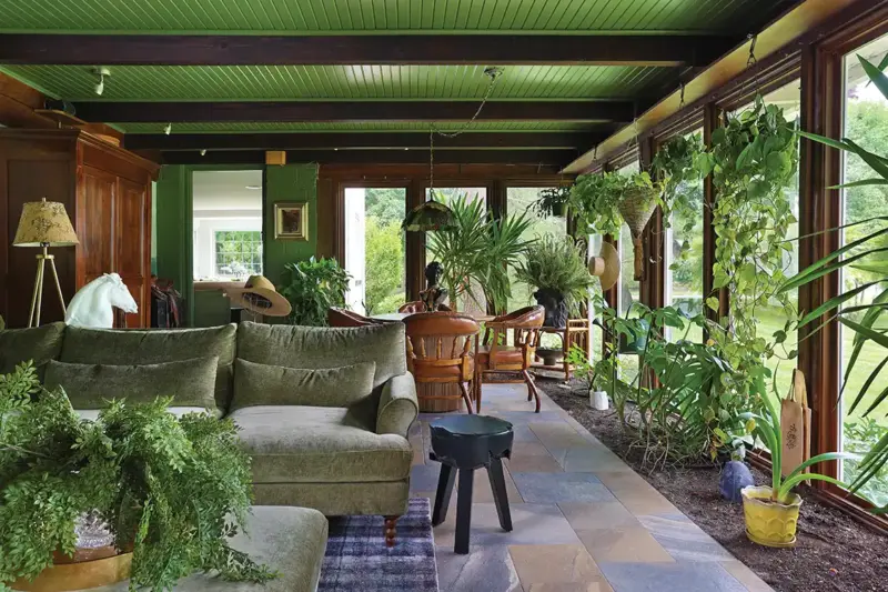 sunroom addition to 1926 Tudor home with hanging plants and green furniture