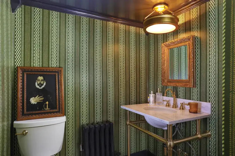 bathroom with green wallpaper with sideways chevron and framed art of Shakespearean era man
