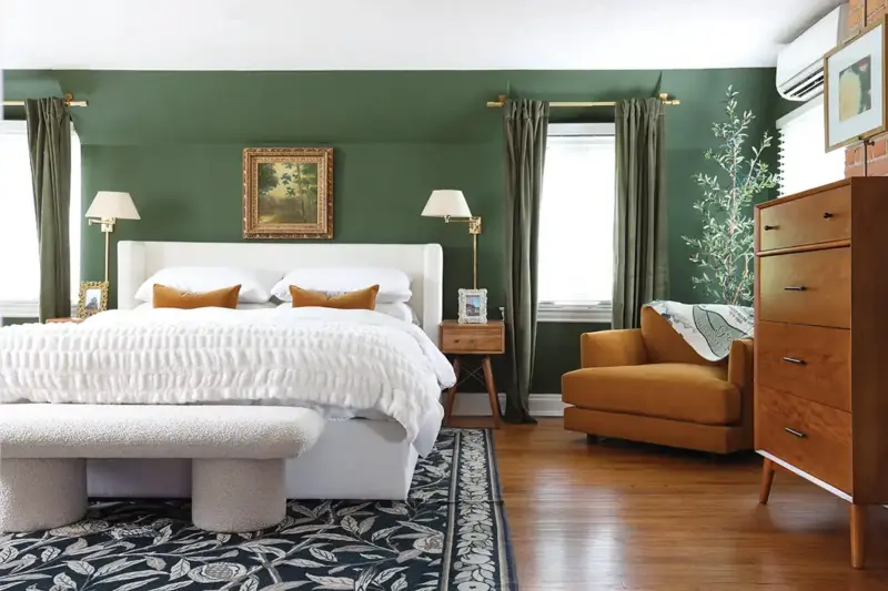 green bedroom with white bedding, saffron armchair and black and white botanical rug