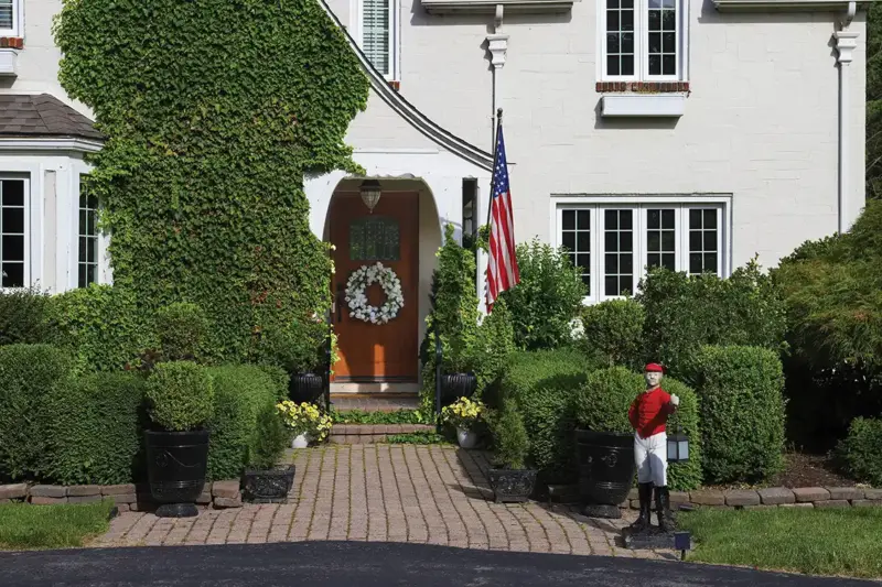 exterior view of 1926 Tudor home with floral wreath flag and sculpture of man holding a lamp